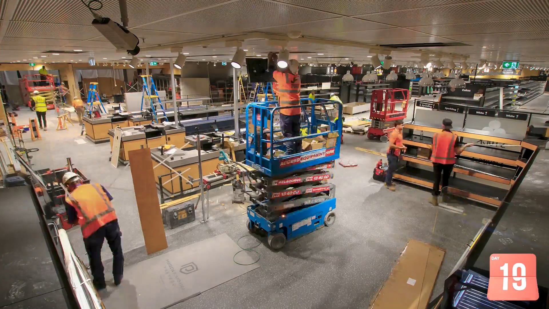 Interior construction of an ALDI supermarket showing refurbishment works with exposed ceiling, lighting installation, shelving frames, and unfinished flooring.