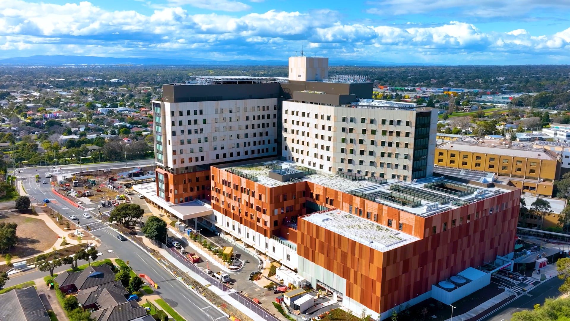 Aerial drone view of Frankston Hospital showing multiple connected buildings, car parks, and surrounding urban landscape under clear skies.